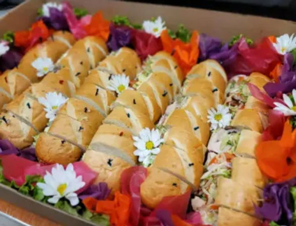 Assorted mini sandwich rolls neatly arranged on a catering tray, filled with deli-style fillings and garnished with colorful edible flowers and daisies — vibrant party platter