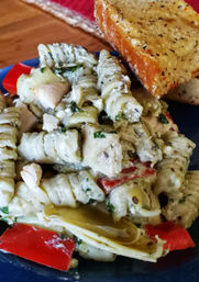 Creamy pesto rotini pasta with artichoke hearts, roasted red peppers and diced chicken, served with garlic-herb bread on a blue plate