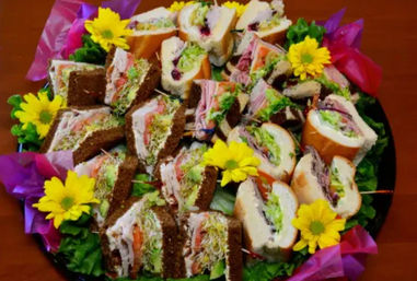Assorted deli sandwich platter of rye and bagel halves filled with turkey, lettuce, tomato and sprouts, garnished with yellow daisies for a catered party.