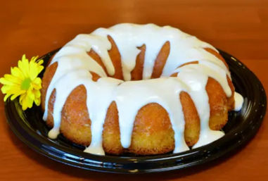 Glazed bundt cake drizzled with white icing on a black plate next to a small yellow daisy on a wooden table.