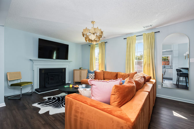 Bright residential living room with orange velvet sectional, TV above white fireplace, light blue walls, zebra rug, yellow curtains and brass chandelier