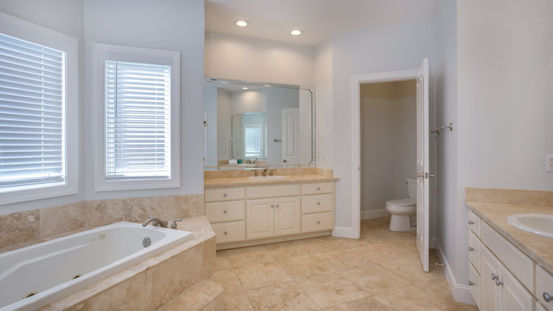 Spa-like bright master bathroom with marble tile floors, built-in soaking tub, large mirrored vanity with recessed lighting and a separate toilet room