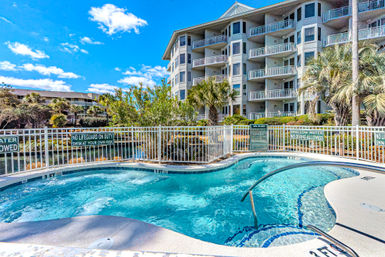 Sunny waterfront condominium complex with an inviting bubbling spa pool, curved handrail, palm trees and stacked balconies under a bright blue sky