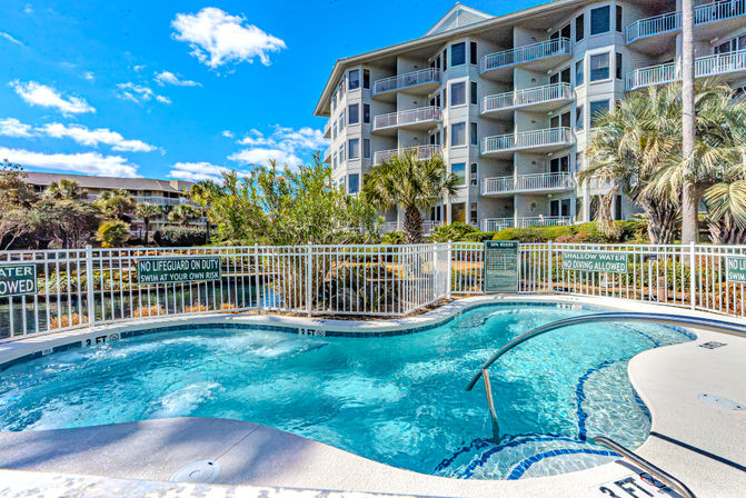 Sunny waterfront condominium complex with an inviting bubbling spa pool, curved handrail, palm trees and stacked balconies under a bright blue sky