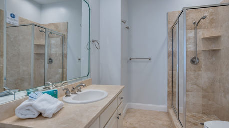 Bright modern bathroom with beige marble-tiled glass shower, single-sink vanity, large mirror and folded white towels, neutral spa-ready palette.