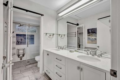 Bright modern master bathroom with white double-sink marble vanity, large mirror, glass walk-in shower with blue bird ocean tile mural and marble floor tiles