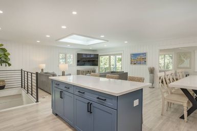 Bright open-concept living space with blue kitchen island and white quartz countertop, wicker bar stools, skylight, gray sofa and adjacent dining area