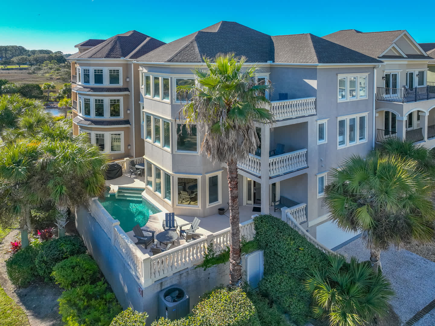 Sunny coastal three-story vacation home with wraparound balconies, palm trees and a private pool overlooking a marsh