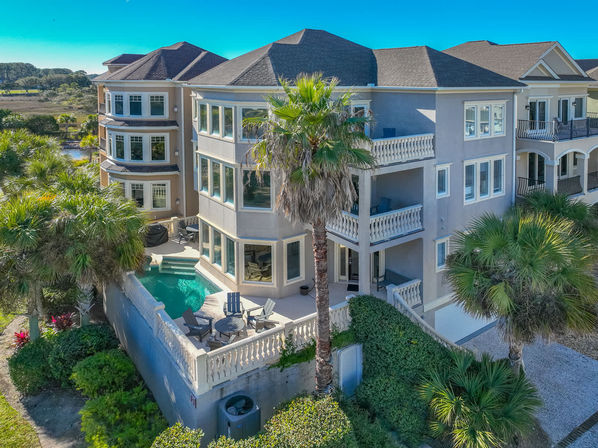 Sunny coastal three-story vacation home with wraparound balconies, palm trees and a private pool overlooking a marsh