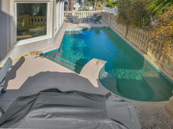 Inviting turquoise backyard swimming pool with built-in spa steps, beige concrete deck, lounge chairs and decorative balustrade framed by palm foliage