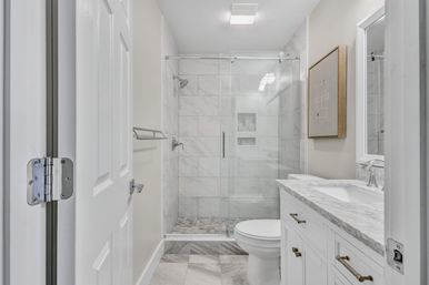 Bright modern residential bathroom with glass sliding-door shower, marble wall and floor tiles, white vanity with marble countertop and chrome fixtures