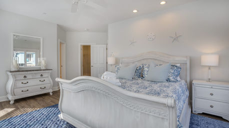 Bright coastal bedroom with white distressed king bed, blue patterned bedding, matching dresser and nightstand lamps, starfish wall accents