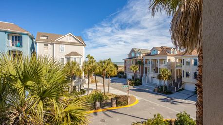 Colorful three-story coastal homes and palm trees lining a sunny seaside street with the ocean visible at the horizon