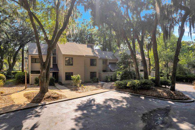 Beige two-story townhouse complex nestled among Spanish-moss-draped live oaks with sun-dappled landscaping, shaded parking and walkways