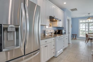 Bright coastal-style kitchen with stainless steel French-door refrigerator, white shaker cabinets, granite countertops, tile floor, electric range and microwave, and a dining nook by a large window