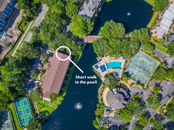 Aerial view of a lakeside residential complex with a circled path and callout 'Short walk to the pool!', showing a blue swimming pool, lake fountain, tennis courts, tree-lined roads and parking.