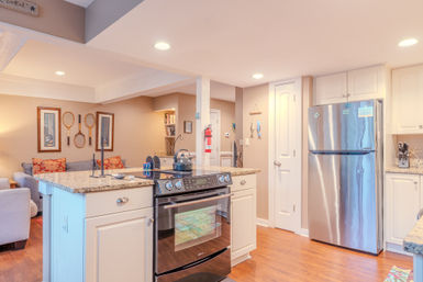 Bright open-plan kitchen and living area with granite island, stainless-steel refrigerator, black range, hardwood floors and coastal decor