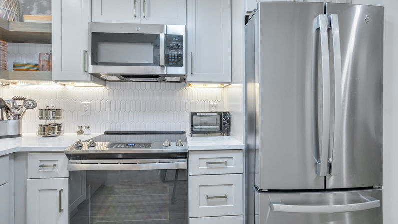 Modern bright kitchen with white shaker cabinets, stainless steel French-door refrigerator, electric range with over-the-range microwave, hexagon tile backsplash, under-cabinet lighting and a countertop toaster oven.
