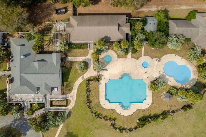 Aerial view of a resort-style estate with three swimming pools, palm-tree landscaping, winding walkways and adjoining buildings.