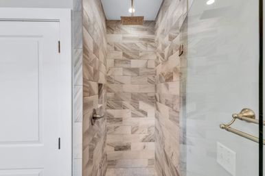 Modern spa-like walk-in shower with gray marble-look subway tiles, overhead square rain showerhead, recessed niche, glass door, and brushed nickel fixtures