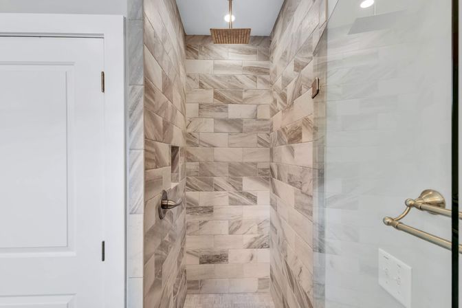 Modern spa-like walk-in shower with gray marble-look subway tiles, overhead square rain showerhead, recessed niche, glass door, and brushed nickel fixtures
