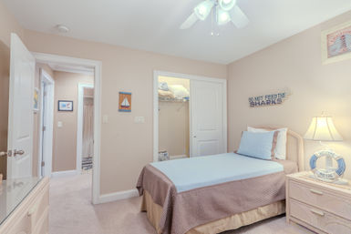 Cozy coastal-themed guest bedroom with twin bed in light blue and beige linens, nightstand lamp and lifebuoy decor, open closet and nautical wall art.