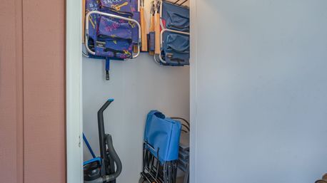 Patio storage closet with folded blue and patterned kids' beach chairs hanging on a rack, stacked folding chairs and a vacuum cleaner—gear ready for a beach day.