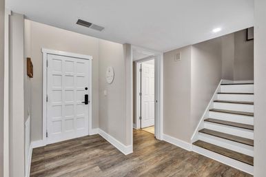 Welcoming modern home entryway with white paneled door, wood-look floors, neutral beige walls, open hallway and staircase with white risers