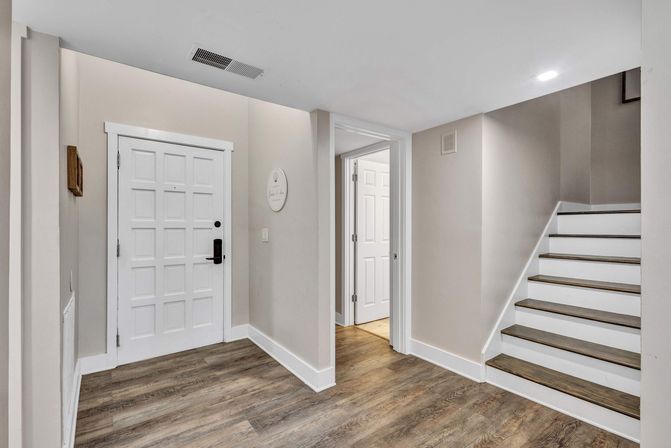Welcoming modern home entryway with white paneled door, wood-look floors, neutral beige walls, open hallway and staircase with white risers