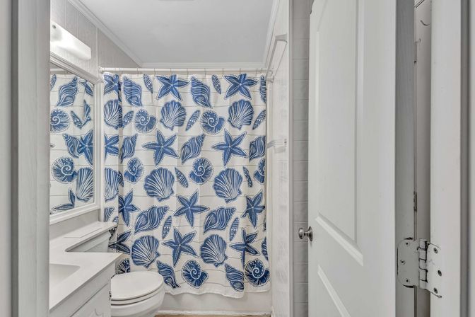 Bright coastal-style bathroom with white vanity and toilet and a playful blue seashell and starfish shower curtain