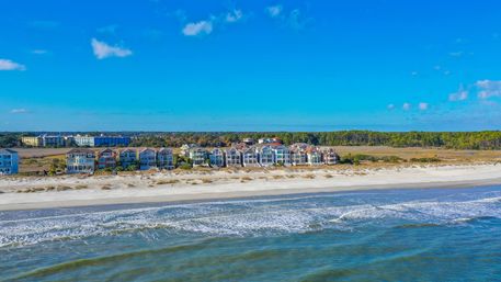 Colorful oceanfront houses lining a sandy beach with gentle waves and a clear blue sky in a seaside coastal community.