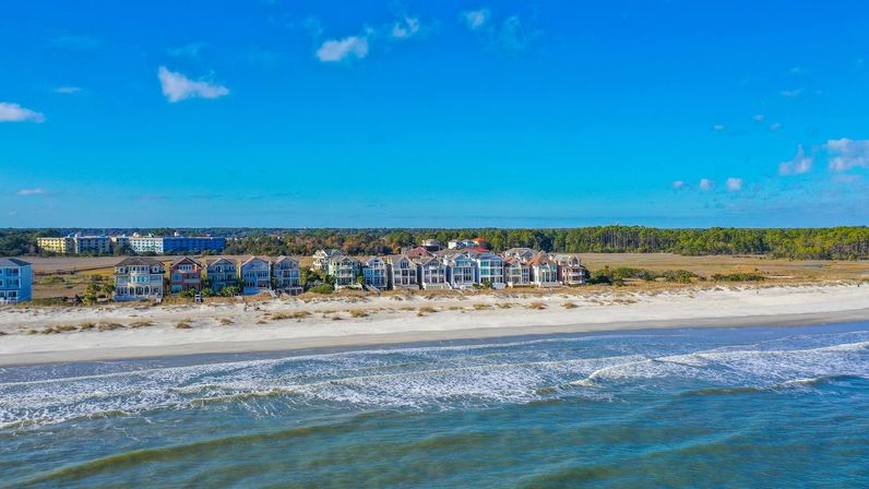 Colorful oceanfront houses lining a sandy beach with gentle waves and a clear blue sky in a seaside coastal community.