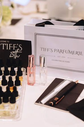 Perfume sampling display with rows of small dropper vials, pink and clear travel roller bottles, and a pen and notebook on a white table — boutique fragrance tasting setup.