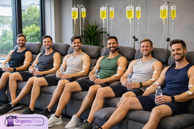 Six fit men seated in reclining chairs at a modern IV hydration lounge, smiling while receiving yellow vitamin IV drips and holding water bottles in a bright wellness clinic with windows and plants.
