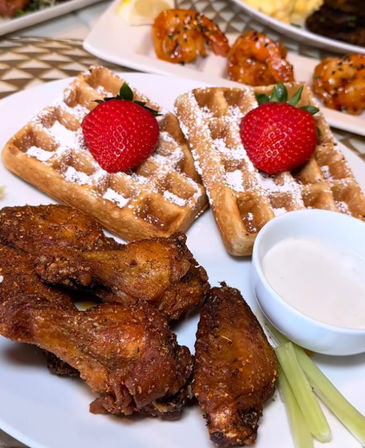 Crispy fried chicken wings with Belgian waffles dusted in powdered sugar and topped with fresh strawberries, served with creamy dipping sauce and celery — brunch plate.