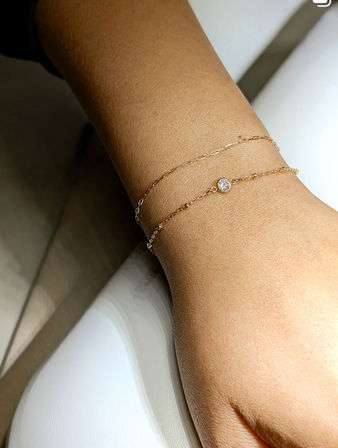Close-up of a wrist wearing two dainty gold chain bracelets, one with a small bezel-set round gemstone, minimalist jewelry close-up.