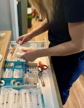 Hands of a healthcare worker organizing syringes, vials, adhesive tape and scissors in a plastic medical supply drawer on a clinic countertop