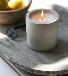 Cozy sunlit kitchen vignette: burning concrete candle on a rustic wooden tray with scissors and a bowl of lemons.