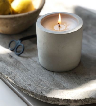 Cozy sunlit kitchen vignette: burning concrete candle on a rustic wooden tray with scissors and a bowl of lemons.