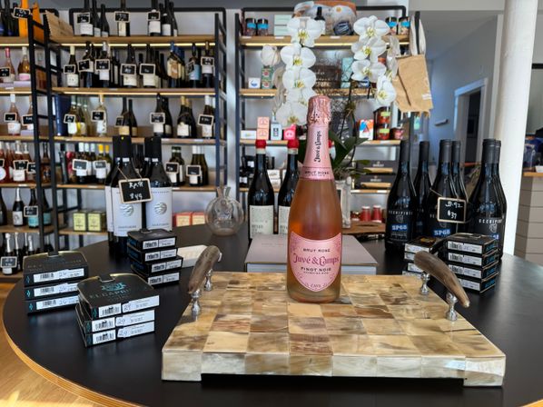 Sparkling Brut Rosé Pinot Noir bottle showcased on a checkered wooden board in a boutique wine shop, surrounded by stacked wine boxes, shelving of bottles and white orchids.