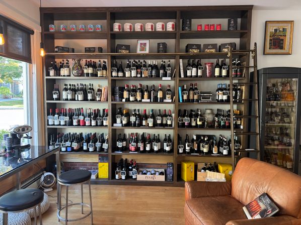 Cozy wine shop interior with floor-to-ceiling wooden shelves of wine bottles, rolling ladder, leather armchair, and stools by a sunlit window