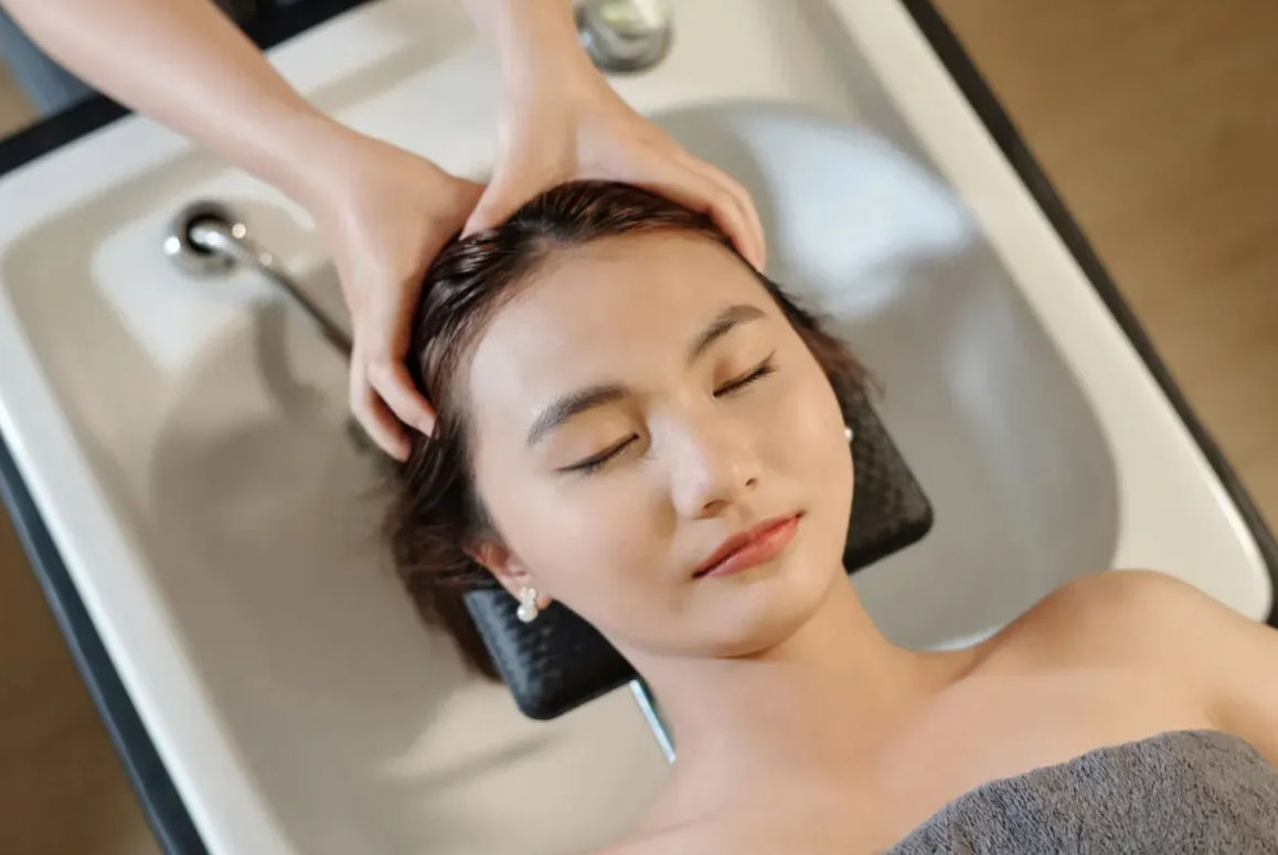 Relaxing salon client with eyes closed enjoying a scalp massage over a shampoo basin