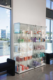 Bright salon interior with glass display case of colorful hair and skincare bottles and tubes on retail shelves by large street-facing windows and black seating