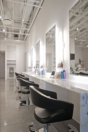 Sleek modern hair salon interior with a row of black styling chairs, marble countertops, backlit mirrors, and neatly arranged hair care products.