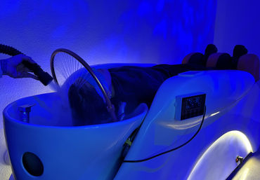 Relaxing scalp steam treatment in a white hydrotherapy spa pod with blue LED mood lighting, digital control panel, neck support and a handheld steaming nozzle