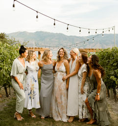 Bridal party of seven laughing together in a vineyard under string lights with mountain views — outdoor wedding vibe