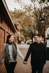Laughing couple holding hands walking on a brick sidewalk in a small downtown with autumn trees, a red brick building and a vintage streetlamp