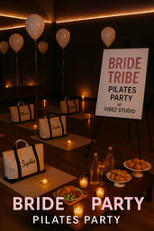 Candlelit bridal “Bride Tribe” Pilates party setup in a dim studio with balloons, yoga mats, personalized canvas tote bags, tea light candles, water bottles and a small pastry and fruit spread.