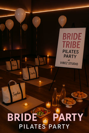 Candlelit bridal “Bride Tribe” Pilates party setup in a dim studio with balloons, yoga mats, personalized canvas tote bags, tea light candles, water bottles and a small pastry and fruit spread.