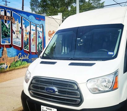 White Ford Transit van parked beside colorful Greetings from Austin mural depicting the Texas Capitol, street scene in Austin, Texas